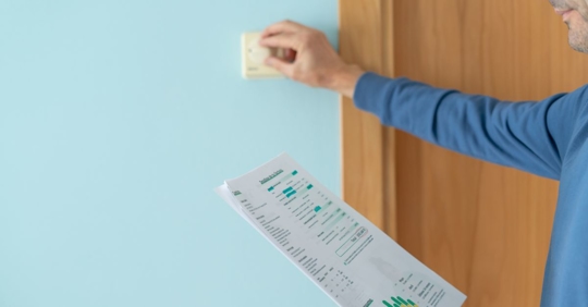 man adjusting thermostat after seeing energy bill